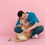 Smiling man in blue shirt hugging a happy dog on pink studio floor, enjoying companionship.